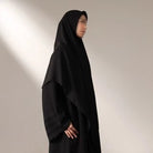 Person wearing a black long hijab by Nehhat Modest against a plain background