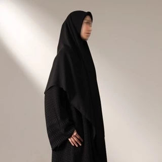 Person wearing a black long hijab by Nehhat Modest against a plain background