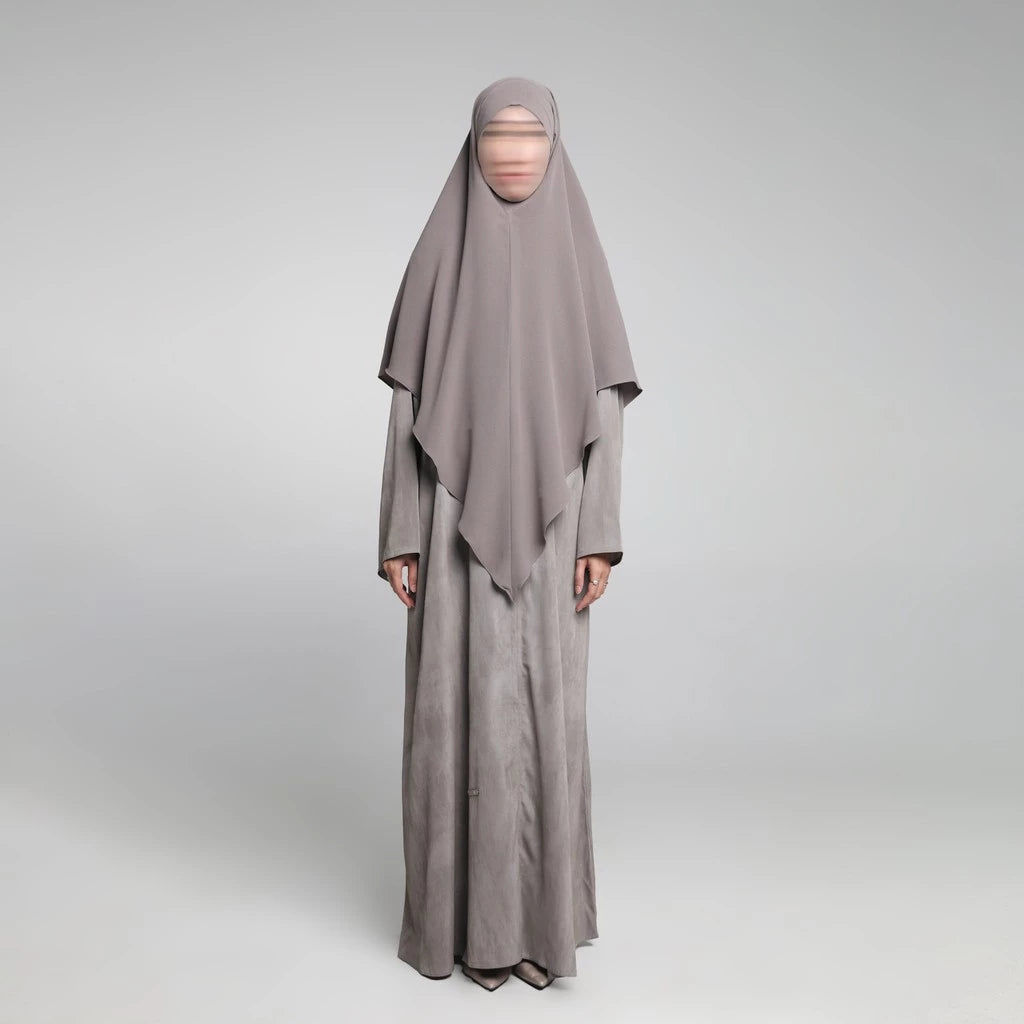 Person wearing a long, light gray Sadda Abaya by Nehhat Modest with a matching headscarf on a white background
