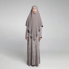 Person wearing a long, light gray Sadda Abaya by Nehhat Modest with a matching headscarf on a white background