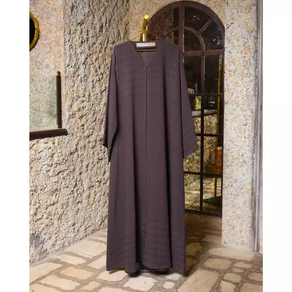 Long dark purple abaya by Nehhat Modest hanging on a stone wall with a mirror.