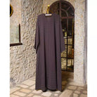Long dark purple abaya by Nehhat Modest hanging on a stone wall with a mirror.