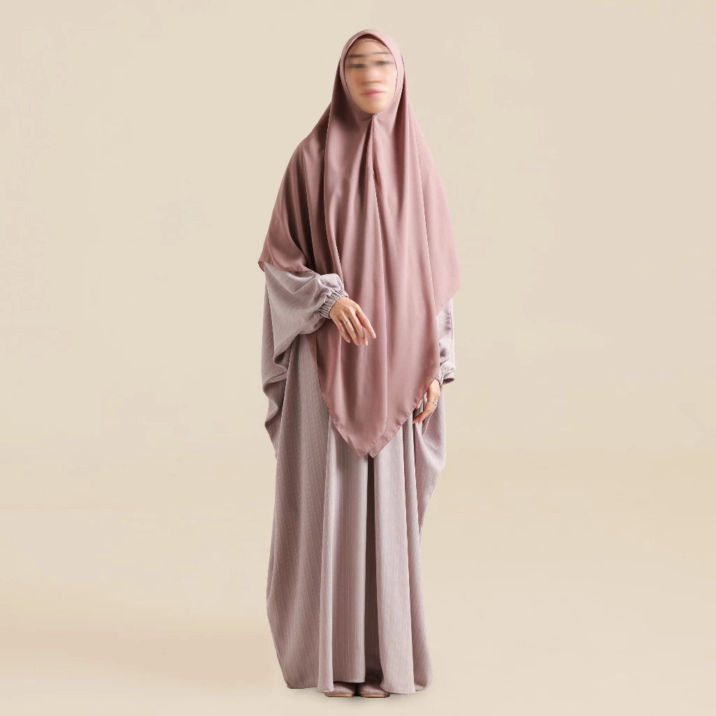 Woman wearing a dusty rose abaya by Nehhat Modest with a matching hijab on a beige background