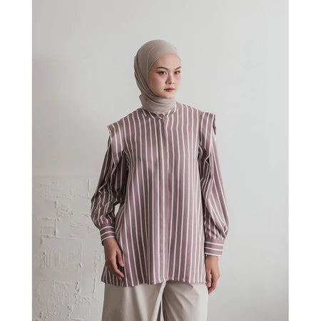 Woman wearing a striped dusty and white shirt by Maima and hijab against a white wall.
