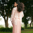 Woman in a peach colored outer by Kartinis Label standing in a park with trees in the background