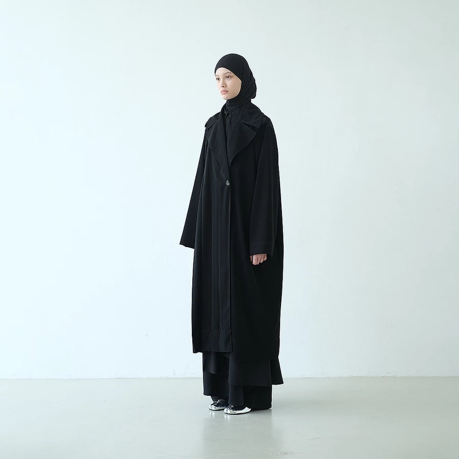 Person wearing a long black coat by Rashawl and headscarf on a white background
