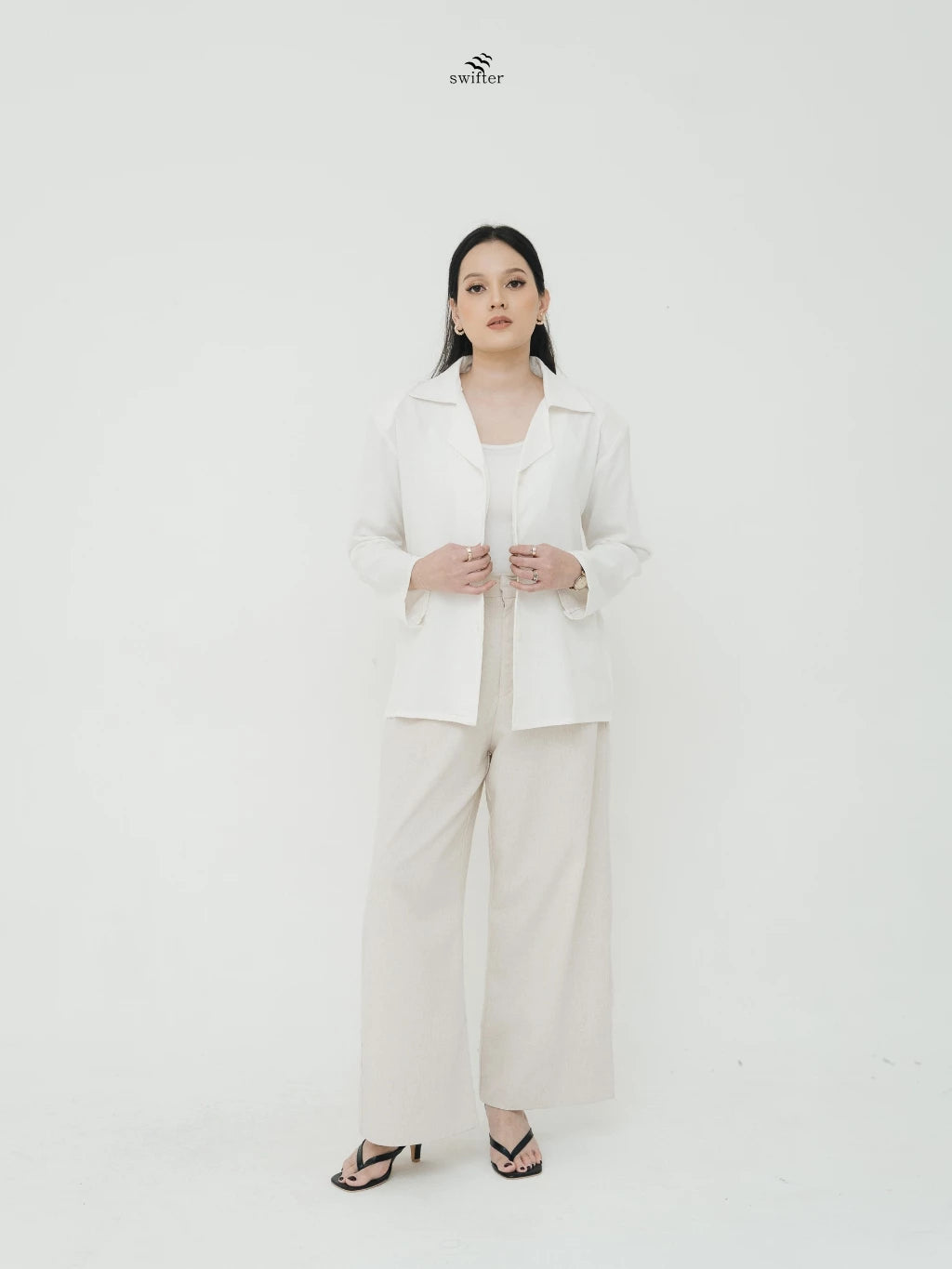 Woman wearing a white blazer by Swifter standing against a white background.