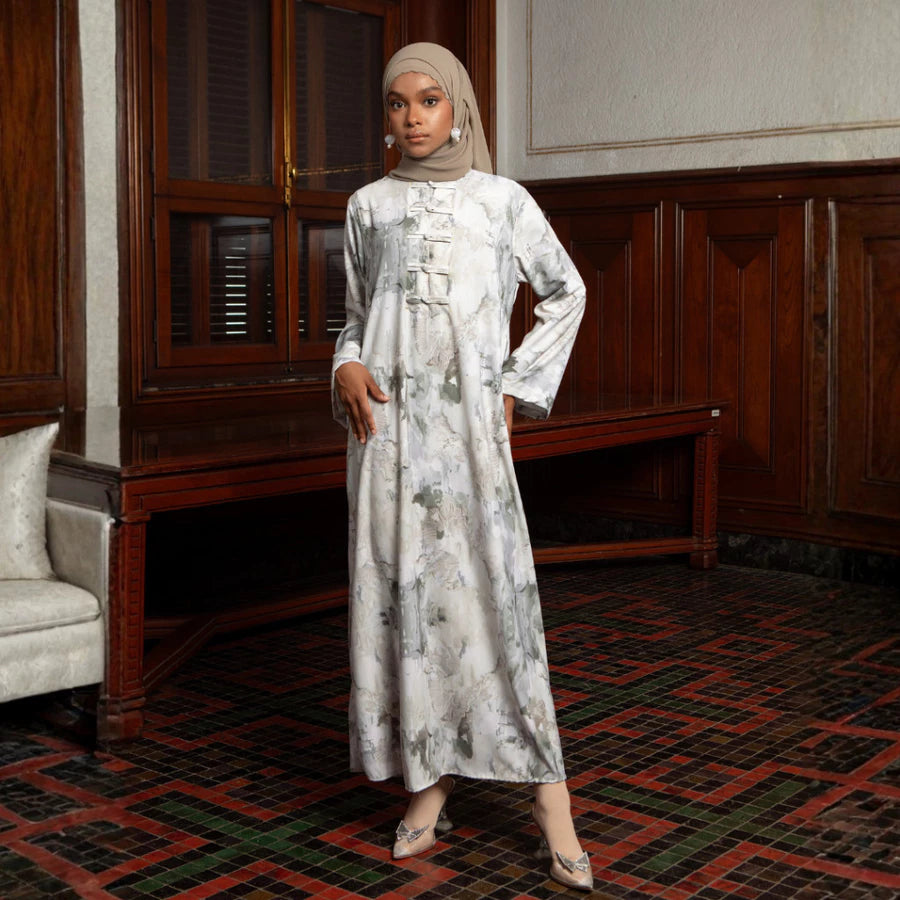 Woman in a long, light-colored dress by Lozy Hijab with floral patterns standing in an elegant room with wooden paneling.