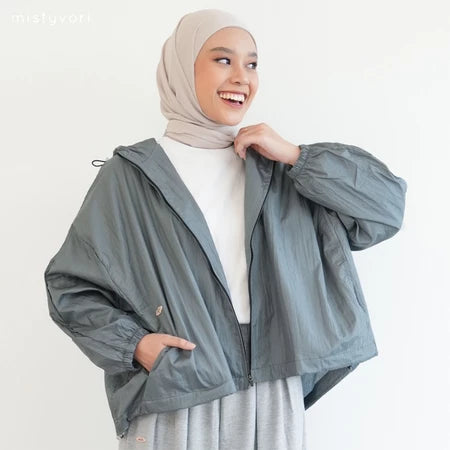 Woman wearing a gray jacket by Mistyvori over a white outfit with a beige hijab on a light background