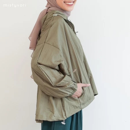 Person wearing a green jacket by Mistyvori with a pink headscarf on a plain background