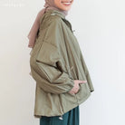 Person wearing a green jacket by Mistyvori with a pink headscarf on a plain background