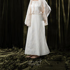 Person wearing a white skirt with lace details against a dark curtain background