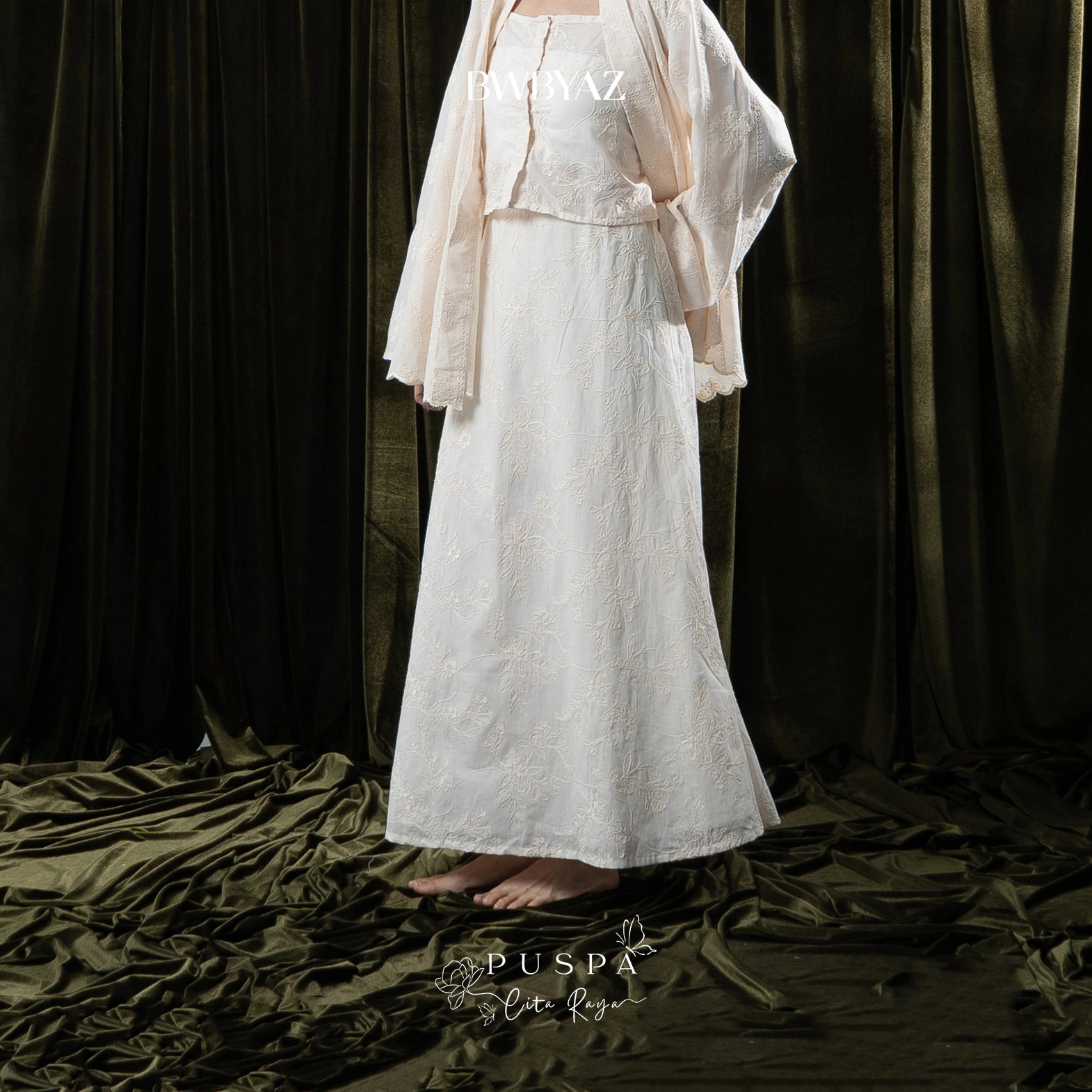 Person wearing a white skirt with lace details against a dark curtain background