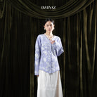 Woman wearing a lavender-colored floral cardigan and white skirt against a dark curtain backdrop with 'BWBYAZ' branding.