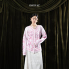 Woman wearing a pink floral cardigan and white skirt against a dark curtain backdrop with 'BWBYAZ' branding.