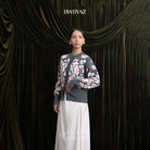 Woman wearing a grey floral cardigan and white skirt against a dark curtain backdrop with 'BWBYAZ' branding.