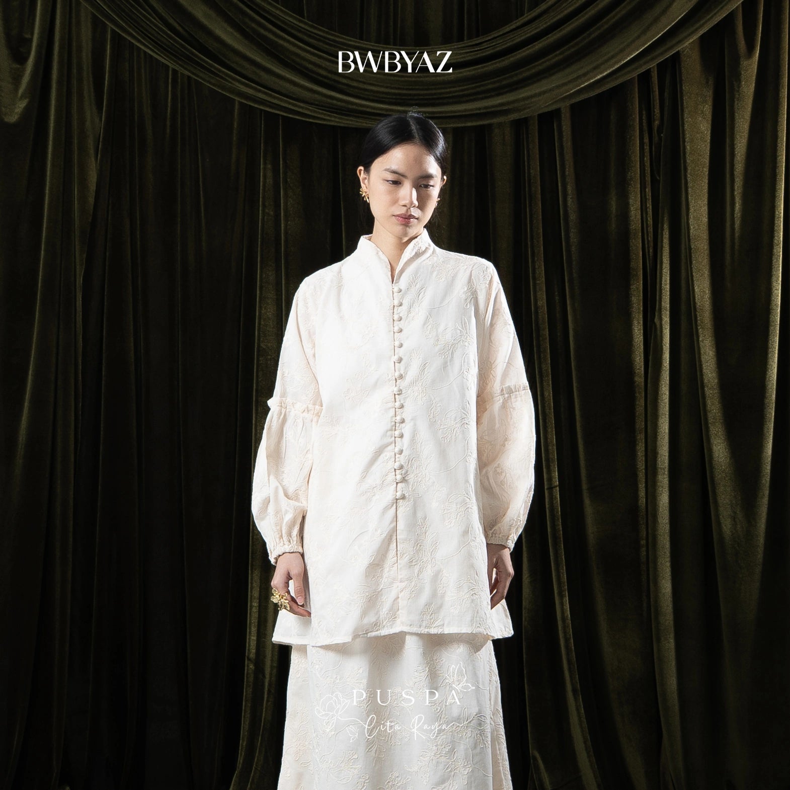 Woman wearing a cream tunic with lace details against a dark curtain backdrop with 'BWBYAZ' branding.

Seorang wanita mengenakan tunik krem dengan detail renda di depan latar belakang tirai gelap dengan merek ‘BWBYAZ’.
