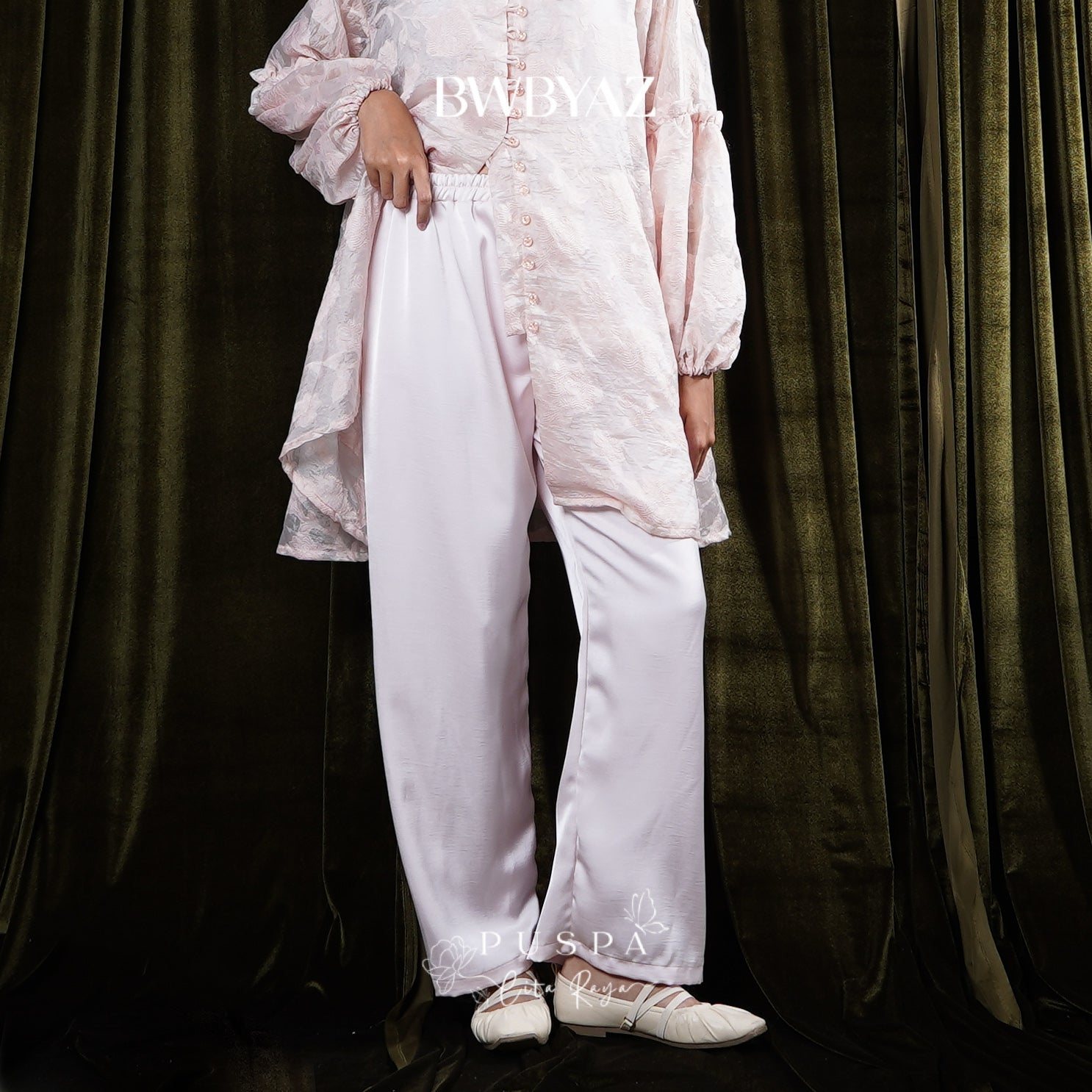 Person wearing a light pink trousers by BWBYAZ against a dark curtain background.
