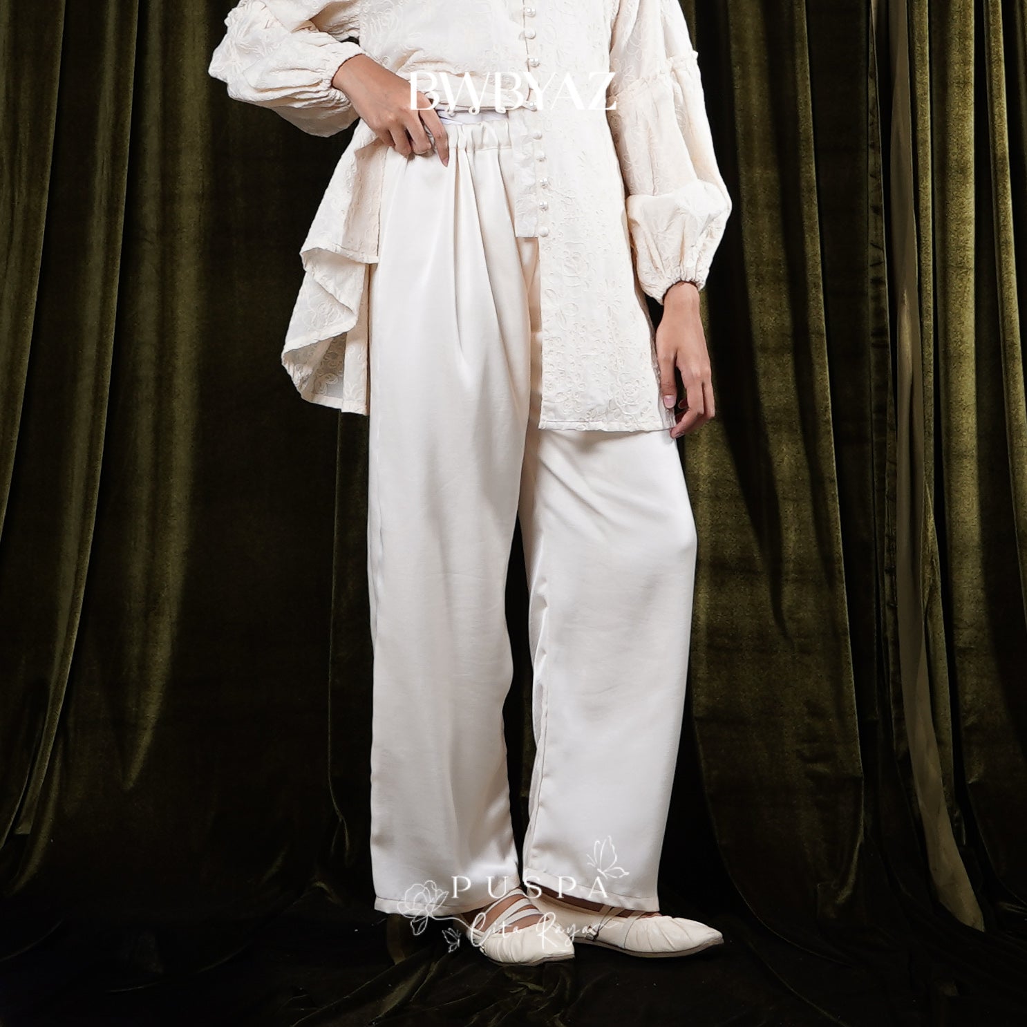 Person wearing a white trousers by BWBYAZ against a dark curtain background