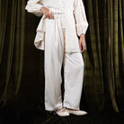 Person wearing a white trousers by BWBYAZ against a dark curtain background