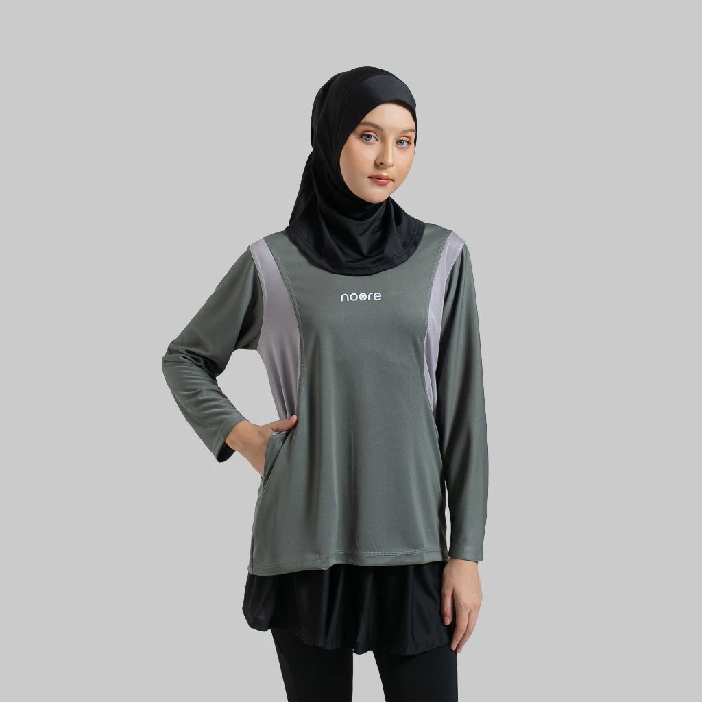 A woman wearing a grey activewear top with the brand name 'noore' on the chest, paired with black bottoms, and a black headscarf.