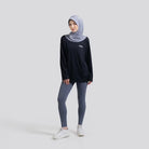 Woman wearing a black long-sleeve top by Noore and gray leggings with a hijab on a white background