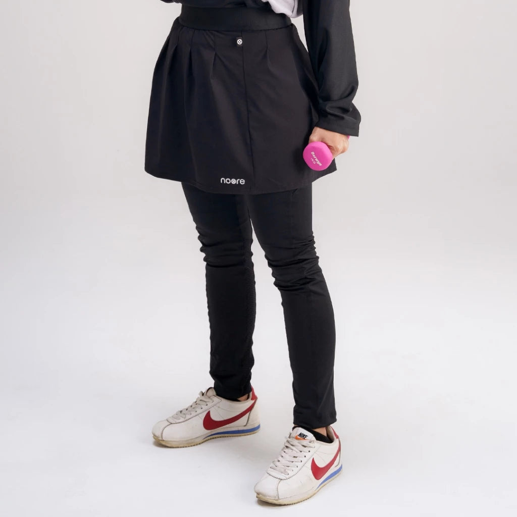 A person wearing a black activewear skirt with the brand name 'noore' visible on the front, paired with leggings and sneakers.