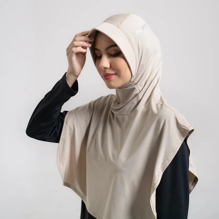 Woman wearing a beige sport hijab by Noore against a plain background.