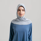 Woman wearing a light gray hijab and blue top from Noore on a plain background