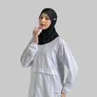 Woman wearing a black sport hijab by Noore and light gray outfit on a plain background