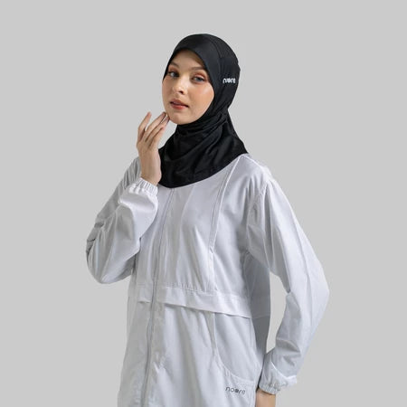 Woman wearing a black sport hijab by Noore and light gray outfit on a plain background
