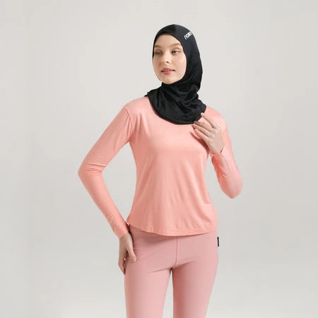 A woman wearing a peach-colored long-sleeve sports inner layer by Noore, designed for comfort and movement, with a black headscarf.