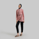 A woman wearing a dusty pink Serenity Burkini by Noore, consisting of a long-sleeved top, bottom, and a detachable skirt, paired with black pants.