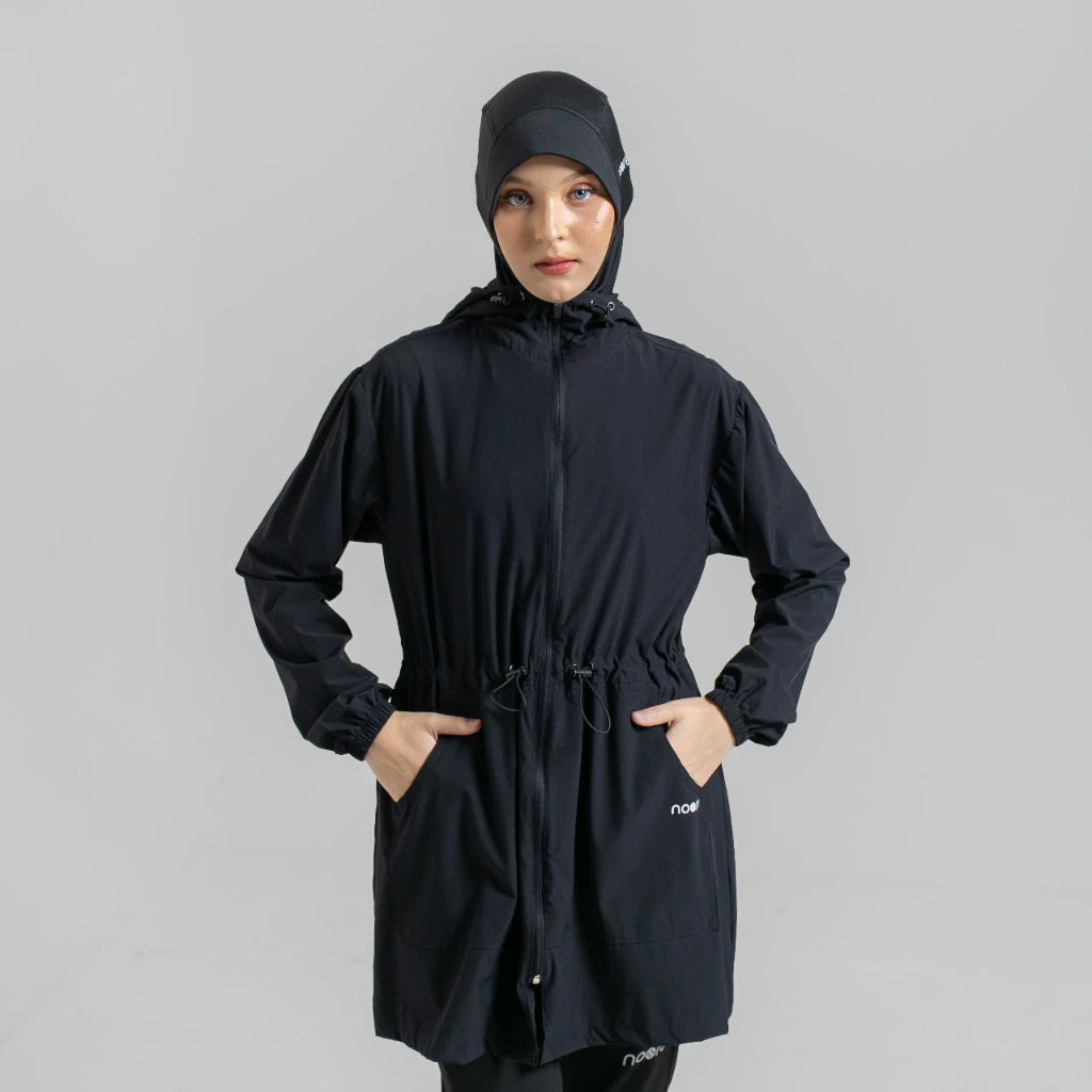 Person wearing a black hooded jacket by Noore on a gray background