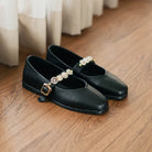 Black flat shoes with pearl embellishments by Dianable on a wooden floor