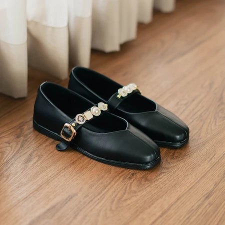 Black flat shoes with pearl embellishments by Dianable on a wooden floor