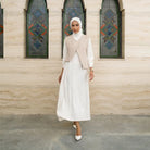 Woman in a white dress by Tunique with a beige vest standing in front of a building with stained glass windows.