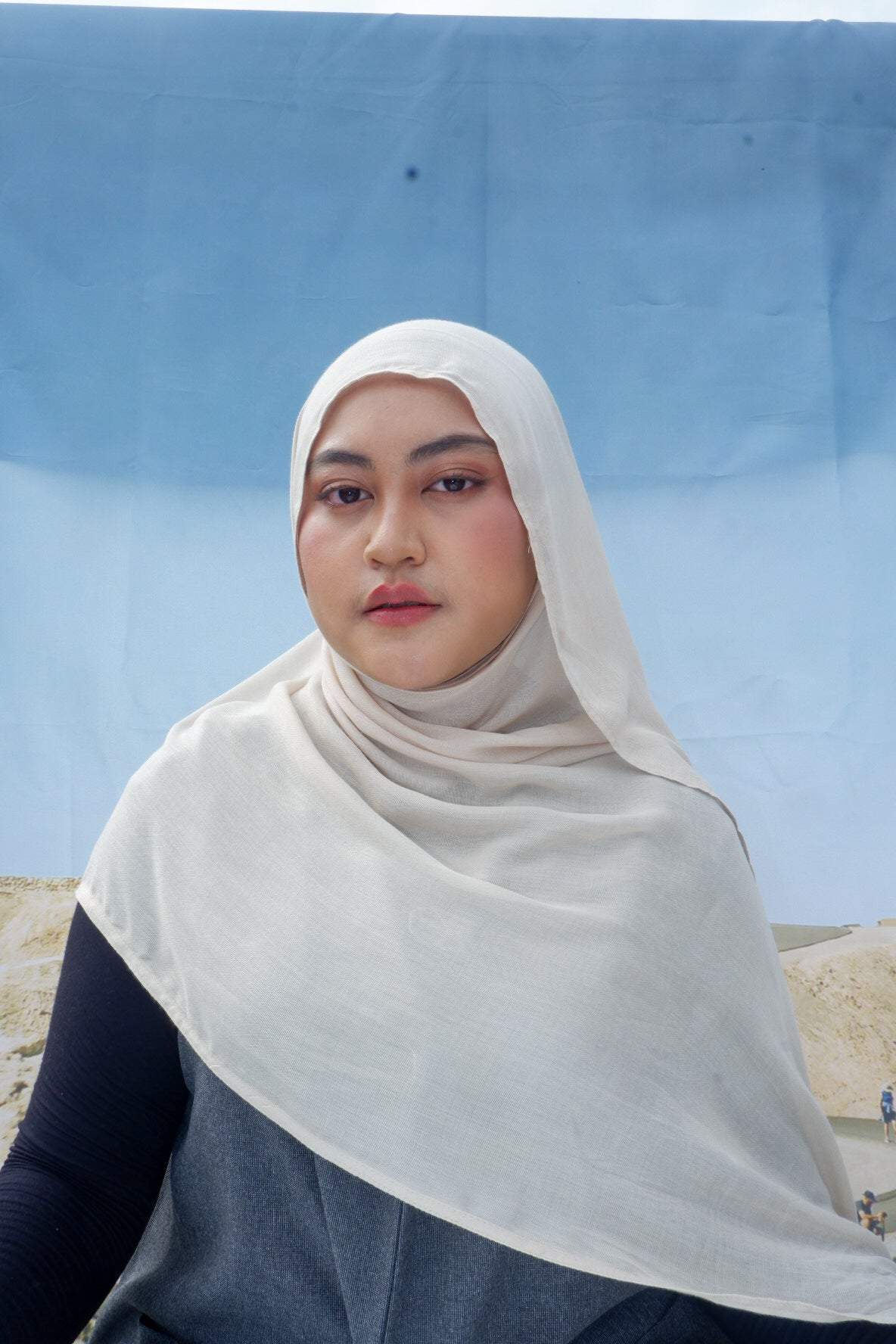 Person wearing a ivory hijab pashmina viscose against a blue sky and desert landscape