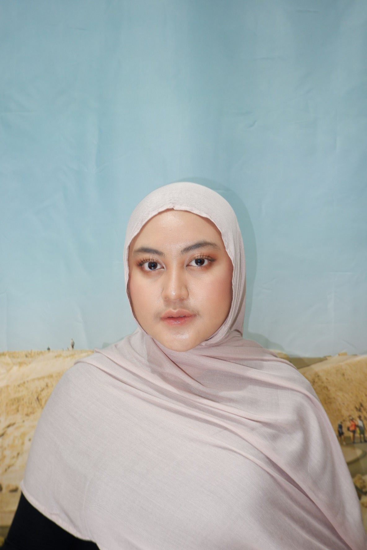 Person wearing a light pink hijab pashmina viscose against a light blue background