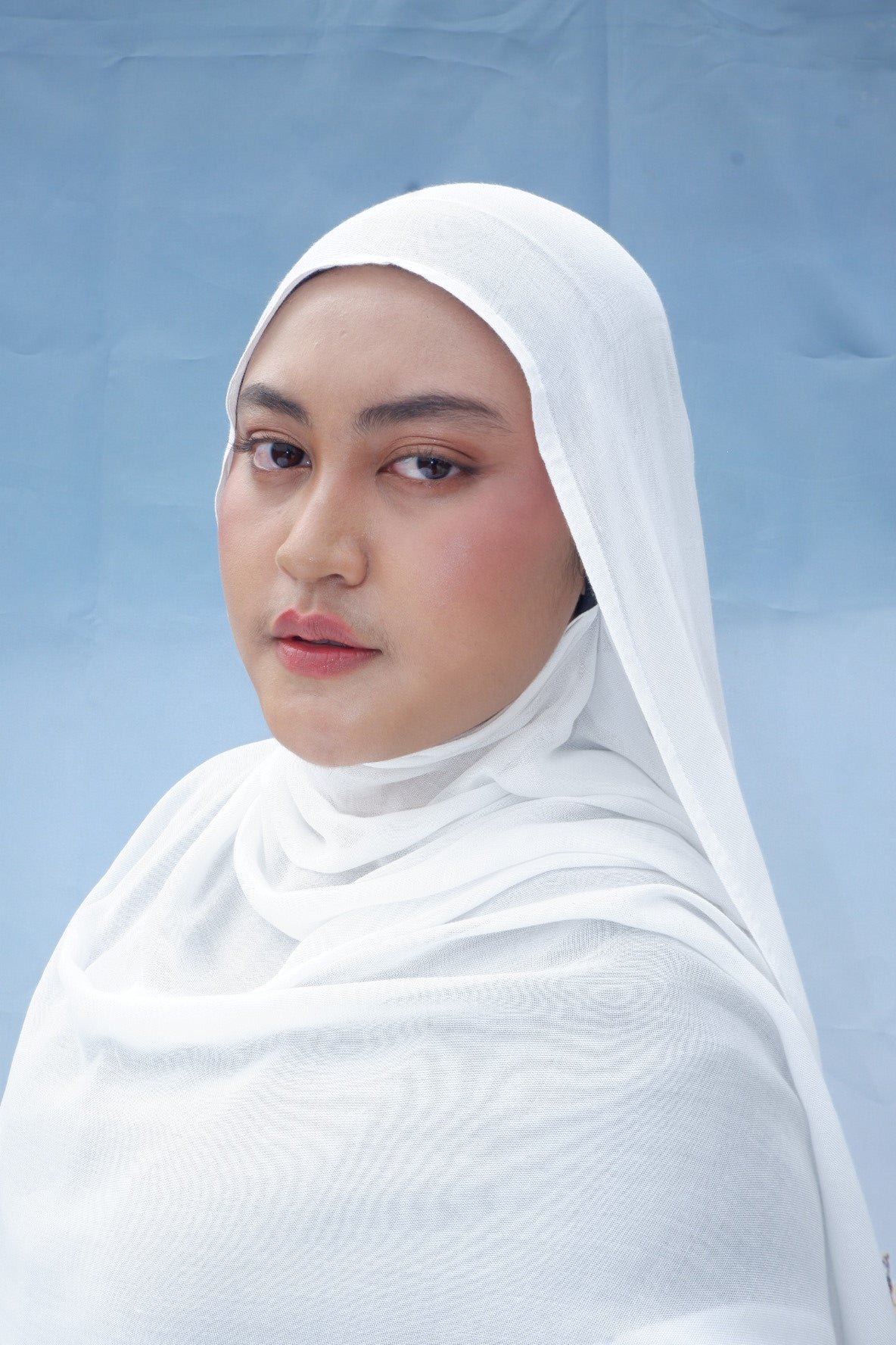 Woman wearing a white hijab pashmina viscose against a light blue background
