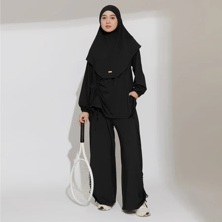 Person wearing a black hijab activewear set by Lozy Hijab holding a tennis racket on a plain background