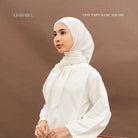 Woman wearing a white hijab by BWBYAZ and blouse against a brown background.