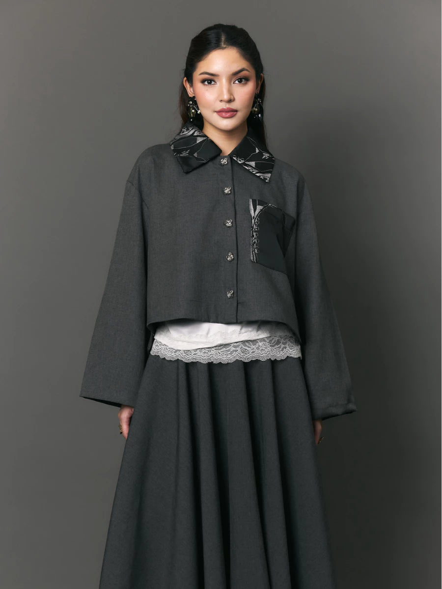 Woman wearing a dark gray outer with patterned collar and pockets by Studio Tui on a gray background
