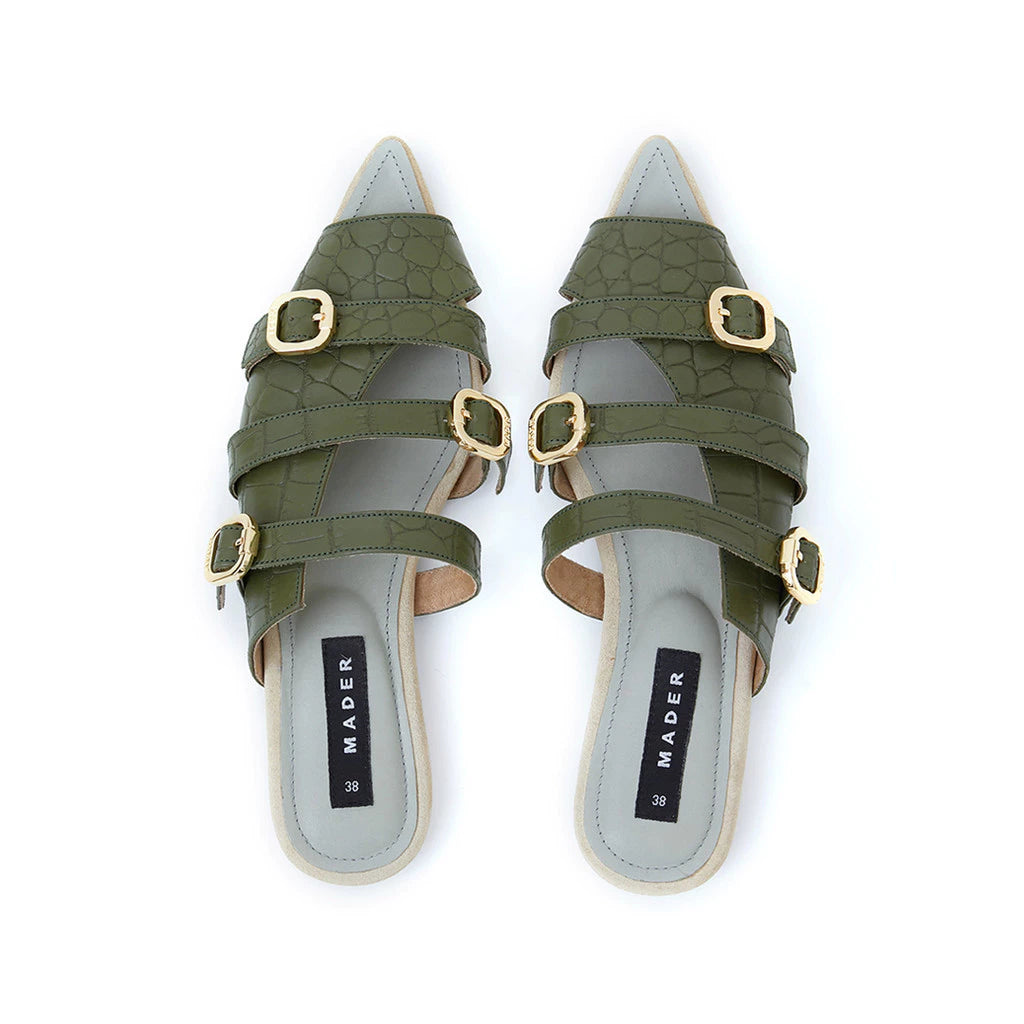 A pair of green crocodile patterned open toe mules with buckle straps and a flat sole.