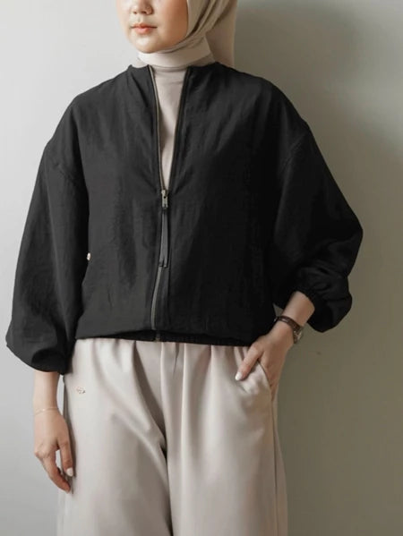 Person wearing a black jacket by Mistyvori and light-colored pants against a plain background