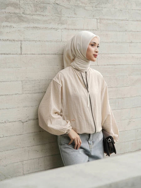 Woman wearing a beige hijab and cream jacket by Mistyvori against a textured wall.