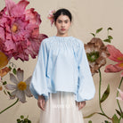 Woman wearing a light blue blouse by BWBYAZ with floral background