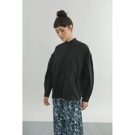 Person wearing a black shirt by Yestoday and patterned pants against a plain background
