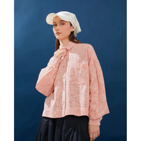 Person wearing a white with pink-textured shirt and white cap against a blue background