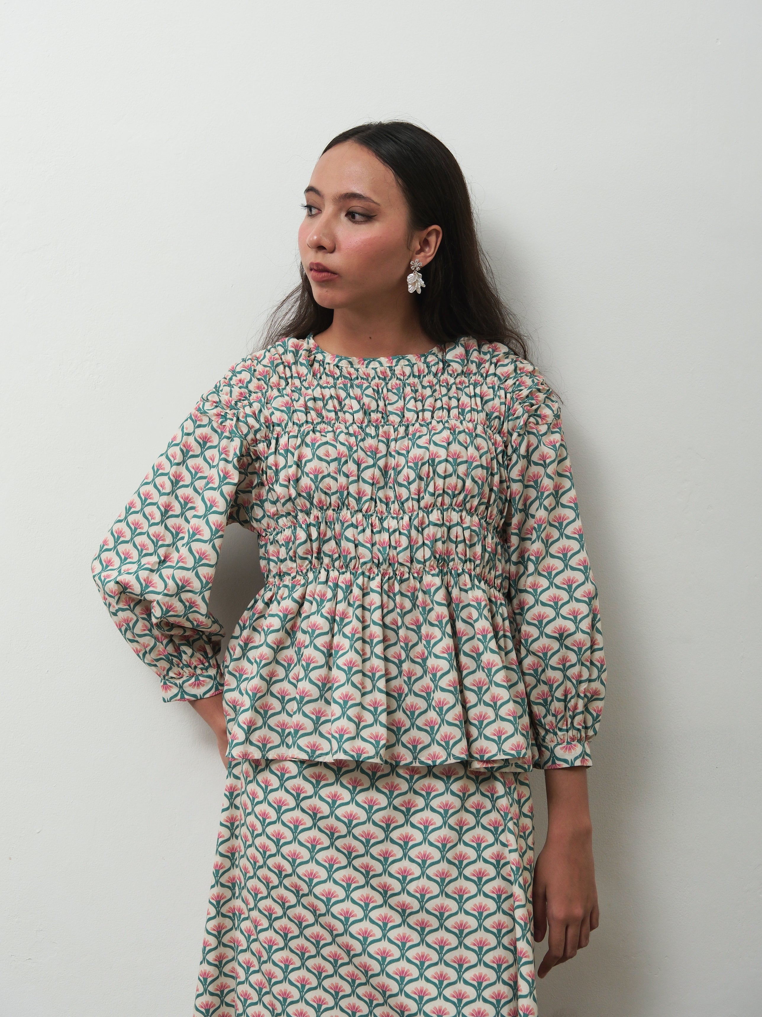 A woman wearing a matching two-piece set by BWBYAZ with a green, pink, and white scallop pattern, standing against a plain light gray wall.